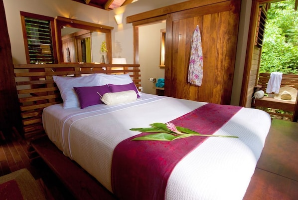 A neatly made bed with a white and maroon bedspread, a wooden headboard, and a wooden bench at the foot of the bed. - Aqua Oceanfront Hotel Resort (Tola)
