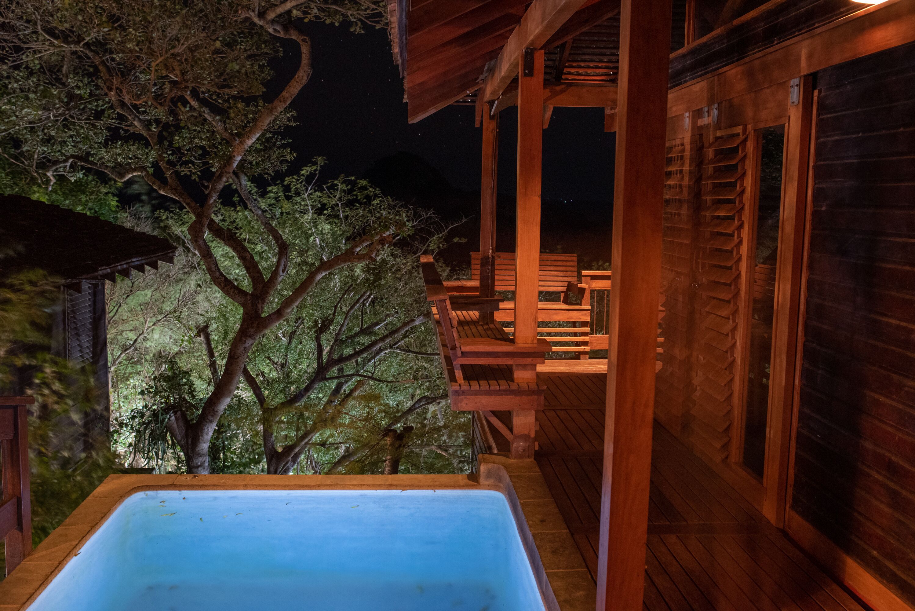 Una terraza de madera con un jacuzzi, sillas de madera y una pérgola.