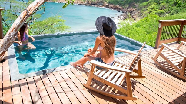 A wooden deck with a hot tub and lounge chairs overlooking a coastal landscape. - Aqua Oceanfront Hotel Resort (Tola)