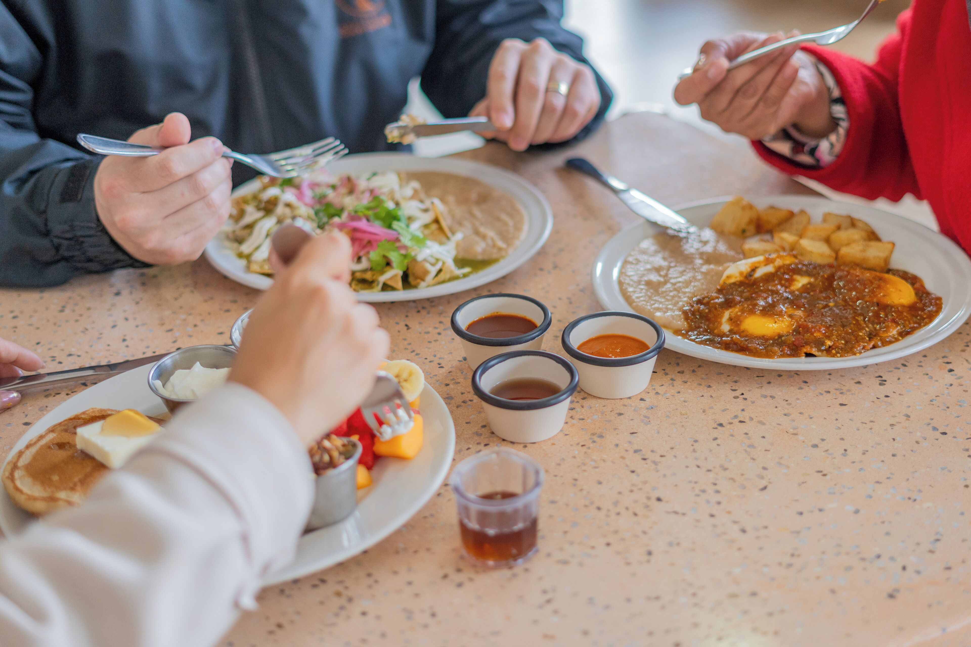 Una mesa de comedor con platos de comida, cubiertos y pequeños recipientes de condimentos.