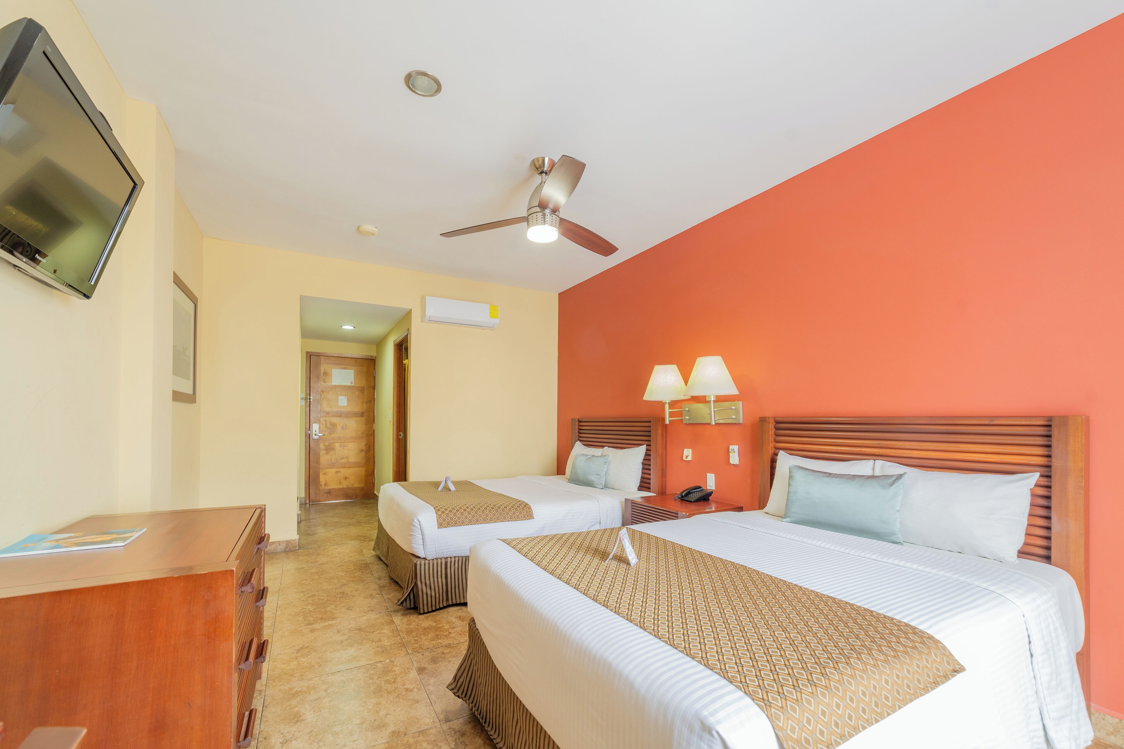 A hotel room with two beds, a desk, a TV, a ceiling fan, and a nightstand with lamps.