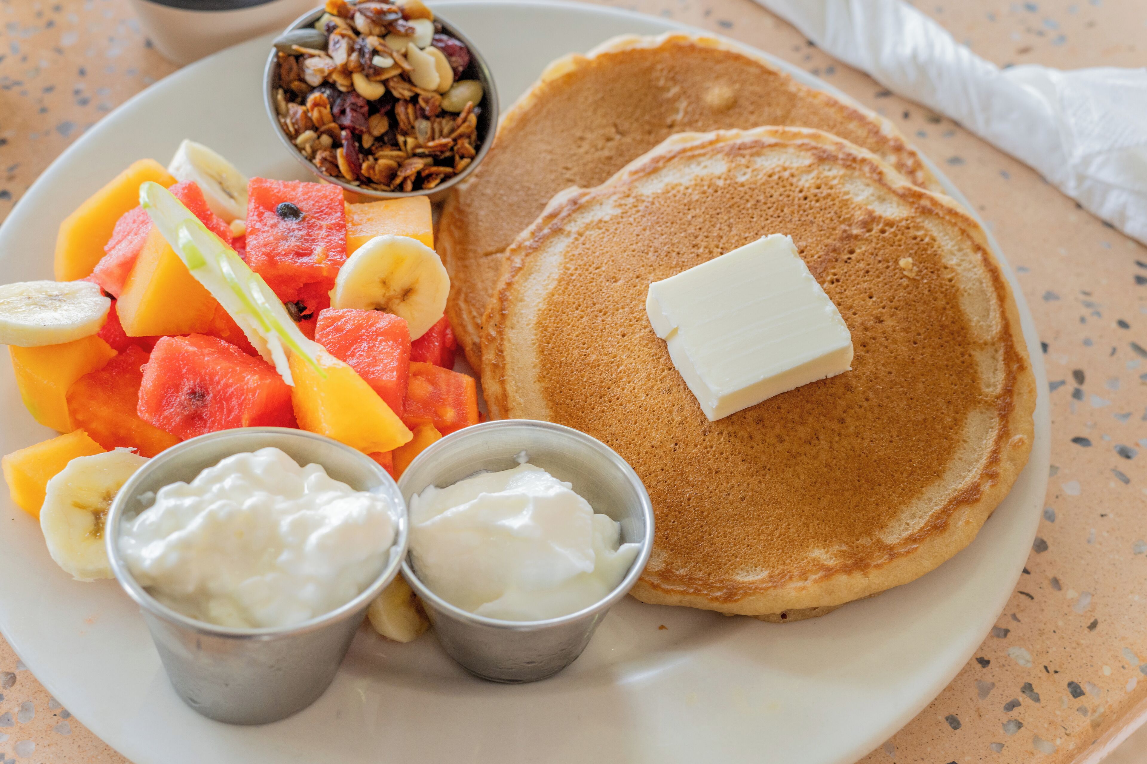 A breakfast plate with pancakes, butter, fruit, and yogurt.