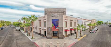 Un hotel con entrada principal, varios balcones y un estacionamiento.