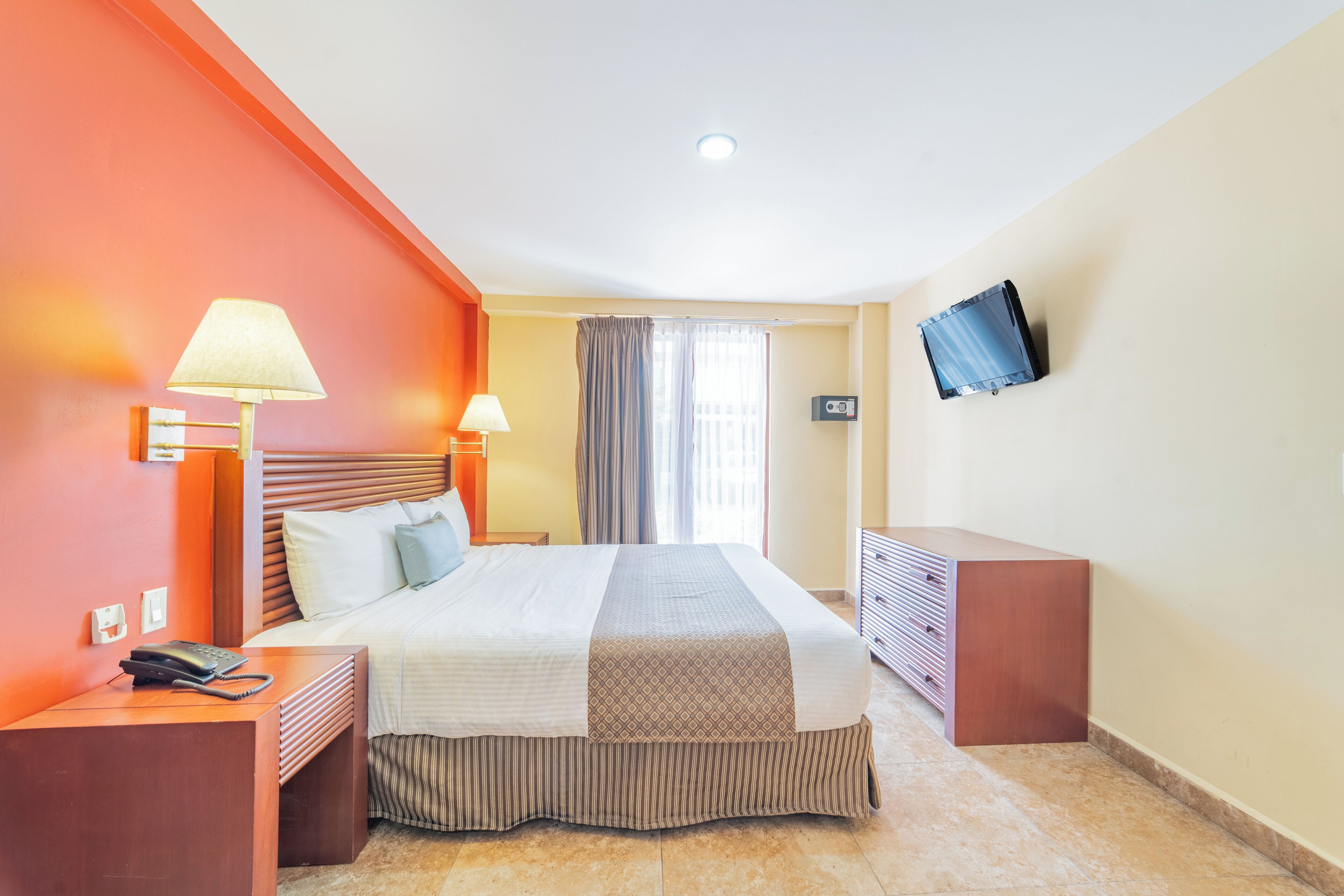 A hotel room with a bed, bedside lamps, a TV, a telephone, and a dresser.