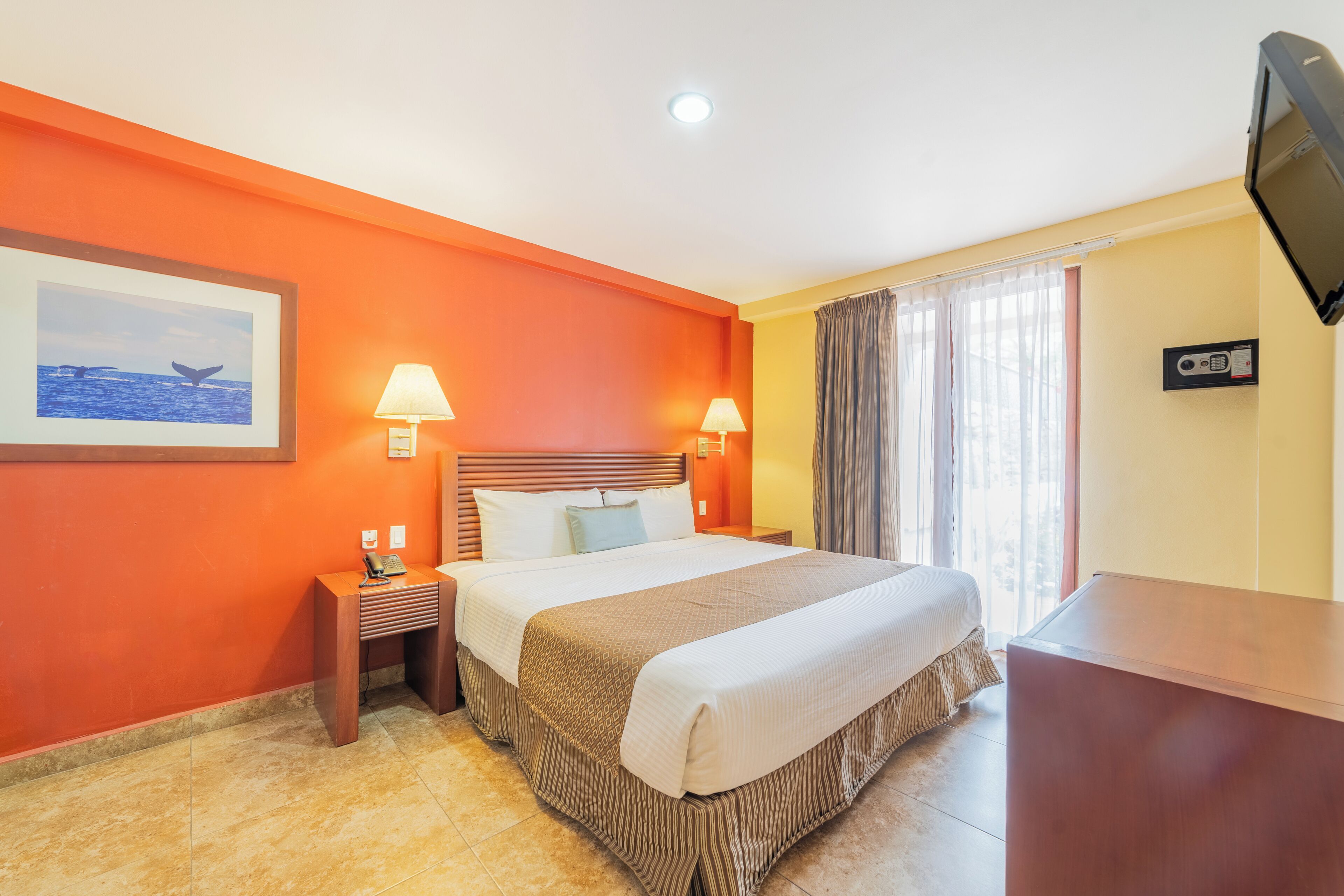 A hotel room with a bed, bedside lamps, a TV, a desk, and a window with curtains.