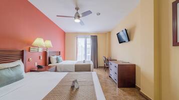 A hotel room with two beds, a desk, a chair, a TV mounted on the wall, and a ceiling fan.
