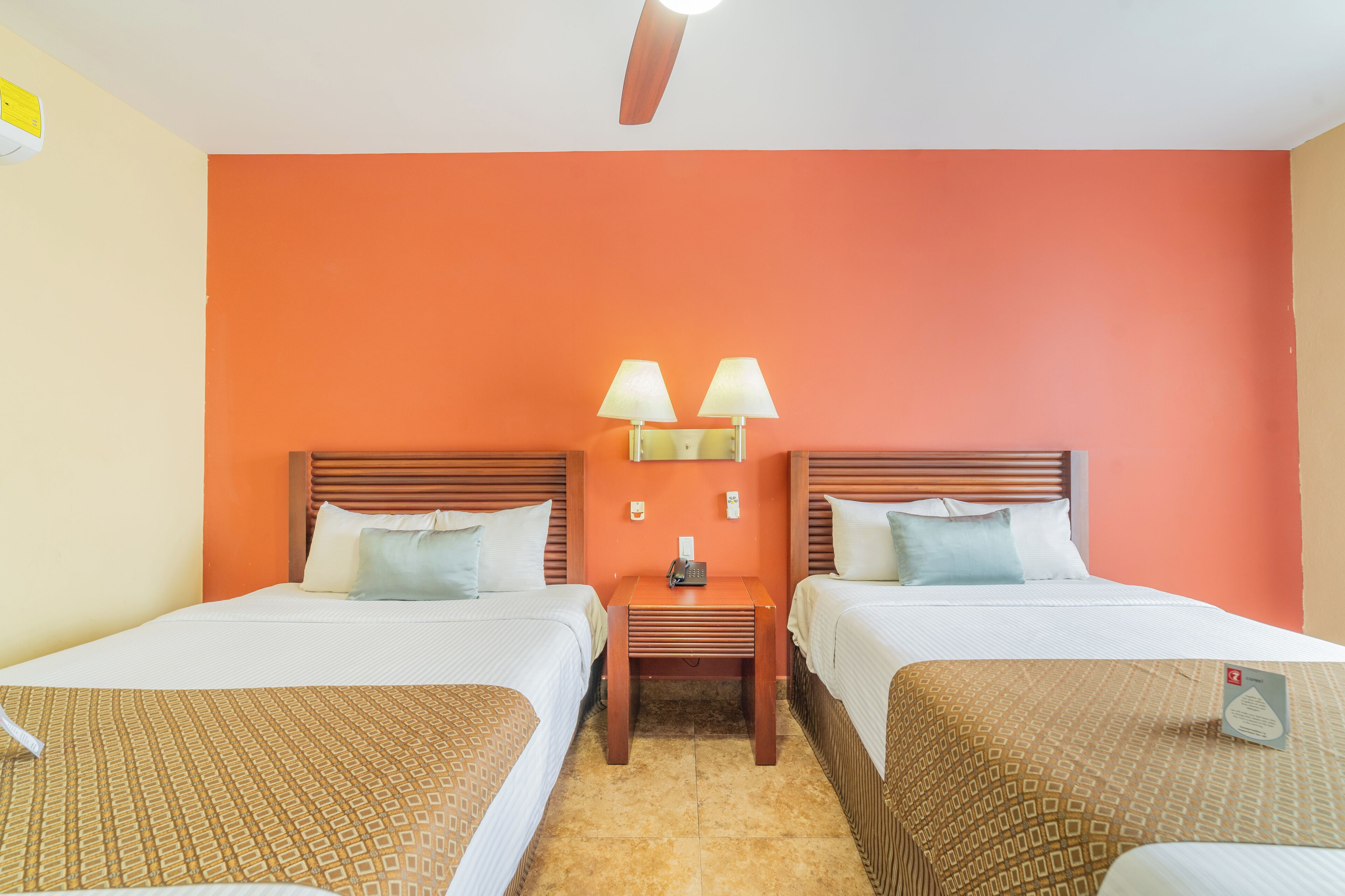 A hotel room with two beds, a nightstand with lamps, and a ceiling fan.
