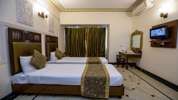 A hotel room with two beds, a desk, a television, and decorative wall panels. - Nahargarh Haveli (Jaipur)
