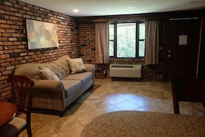 A room with a brick wall, a sofa, a dining table, and a window with curtains. - Chalet Inn & Suites Centerport (Centerport)