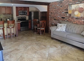 A kitchen with a microwave, refrigerator, and stove. There are two wooden chairs and a sofa with a cushion. The floor is tiled. - Chalet Inn & Suites Centerport (Centerport)