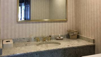 A bathroom with a large mirror, granite countertop, and a sink with gold fixtures.
