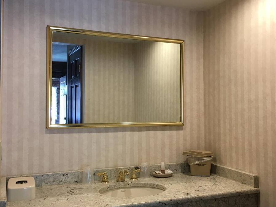 A bathroom with a large mirror, granite countertop, and a sink with gold fixtures.