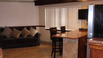 Una sala de estar con un sofá marrón oscuro, cojines estampados, una pequeña zona de bar con taburetes y un televisor montado en la pared.