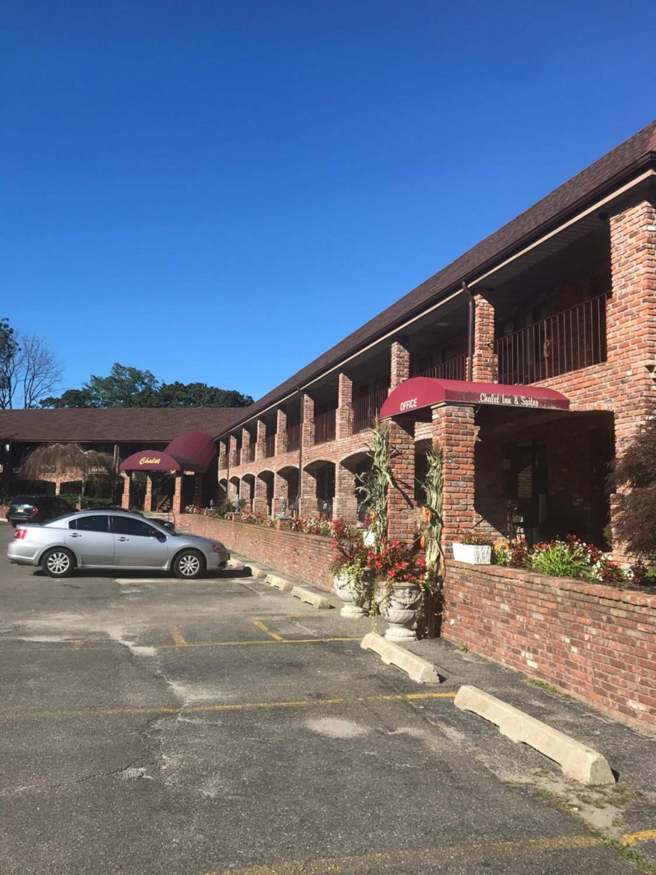 Un bâtiment en briques comprenant plusieurs pièces, un parking et une voiture garée devant.