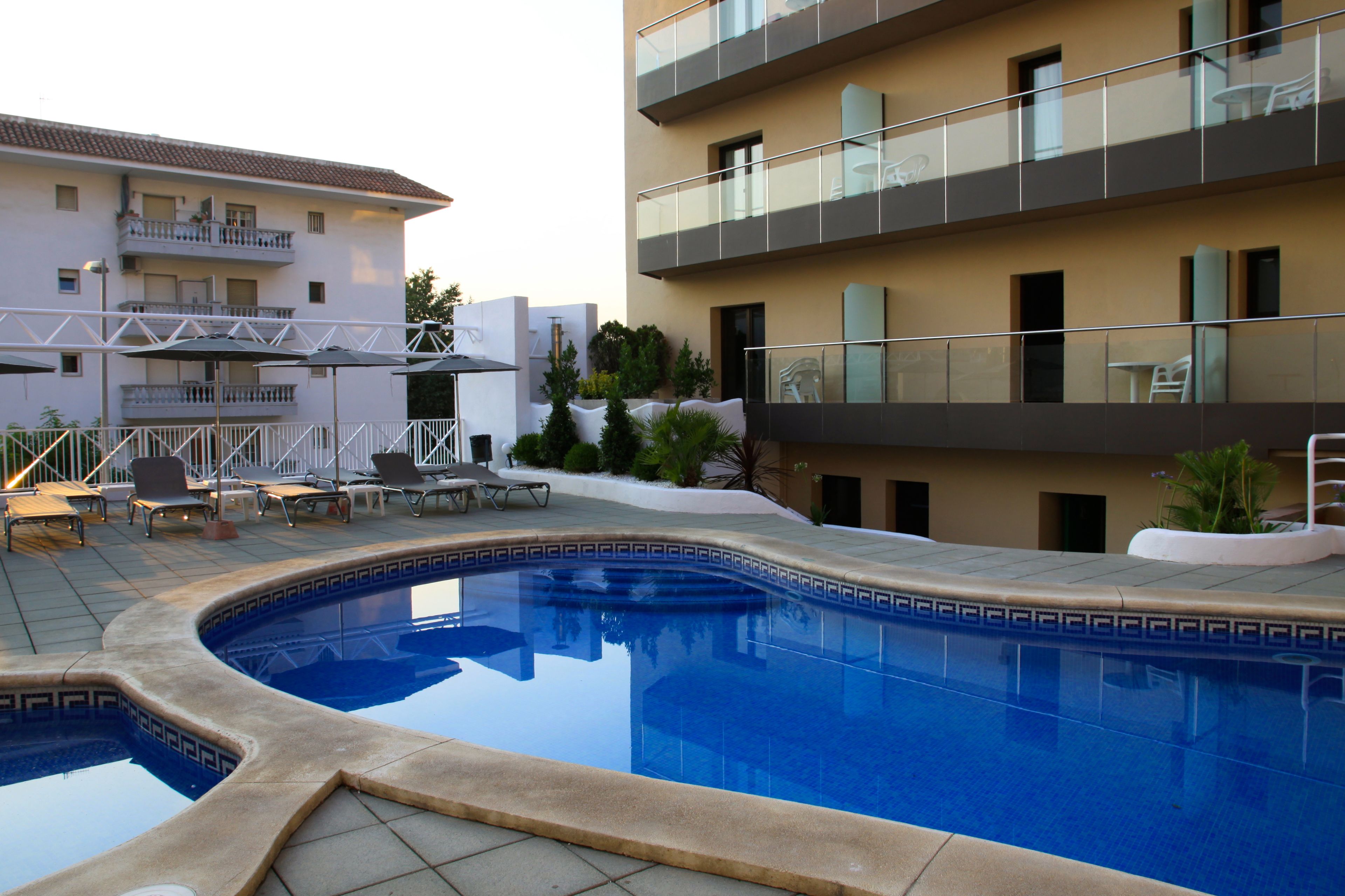 Une piscine dont le carrelage présente un motif géométrique, entourée de chaises longues et de parasols.