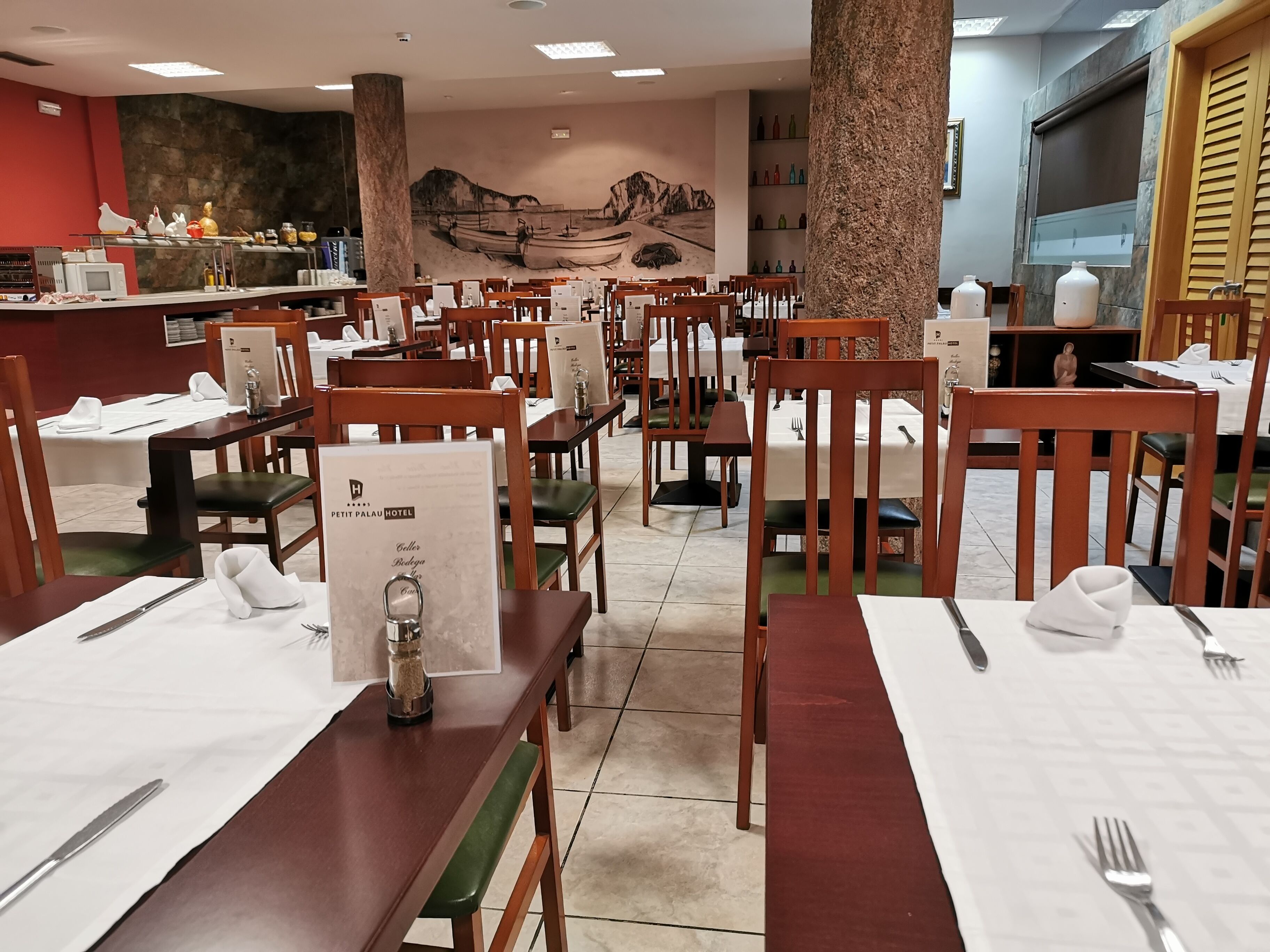 Un restaurante con mesas y sillas de madera, un mural en la pared y una zona de bufé al fondo.