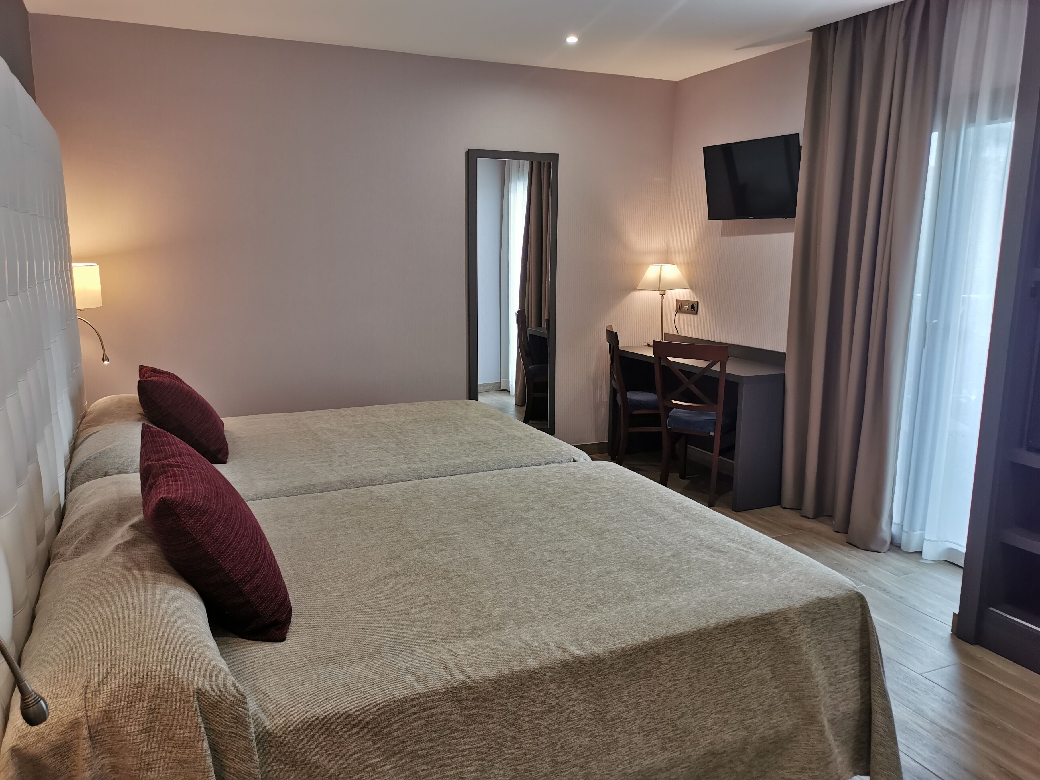 Una camera d'albergo con due letti, una scrivania, una sedia, una televisione e una lampada.
