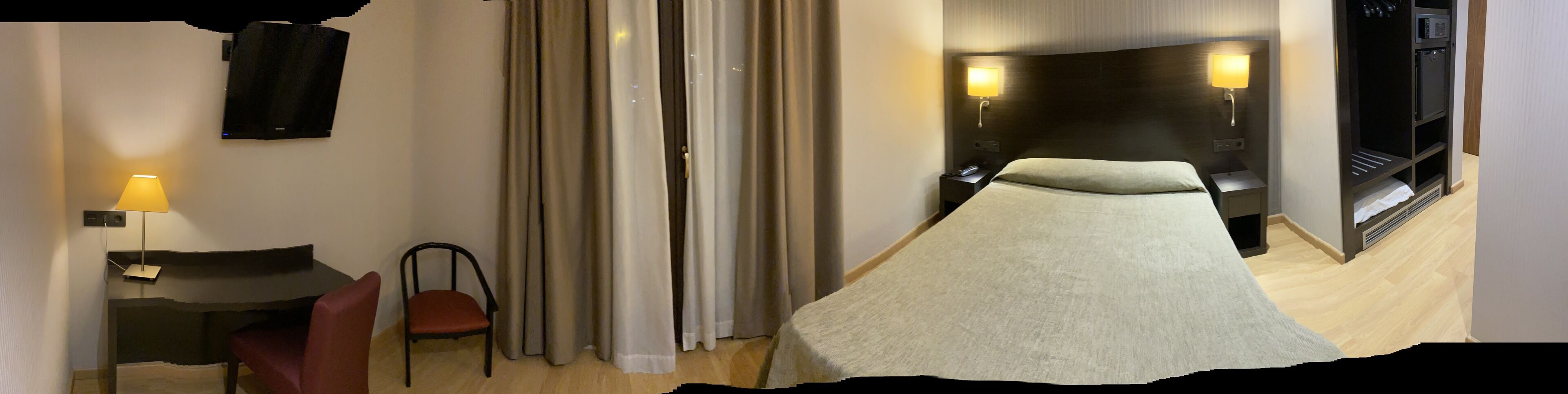 Een hotelkamer met een bed, een stoel, een bureau, een lamp en een gordijn.