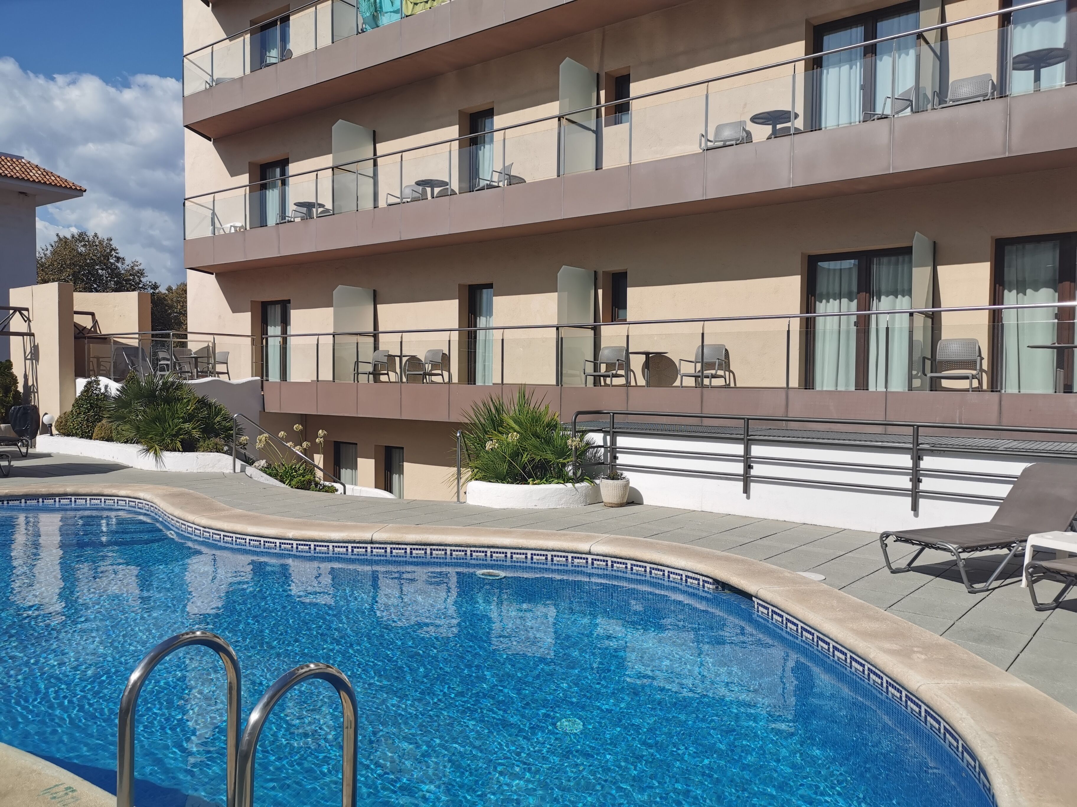 Un hotel con piscina, mobiliario exterior y varios balcones.