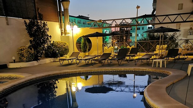 A swimming pool with lounge chairs and umbrellas, surrounded by buildings and greenery. - Petit Palau - Adults Only (Blanes)