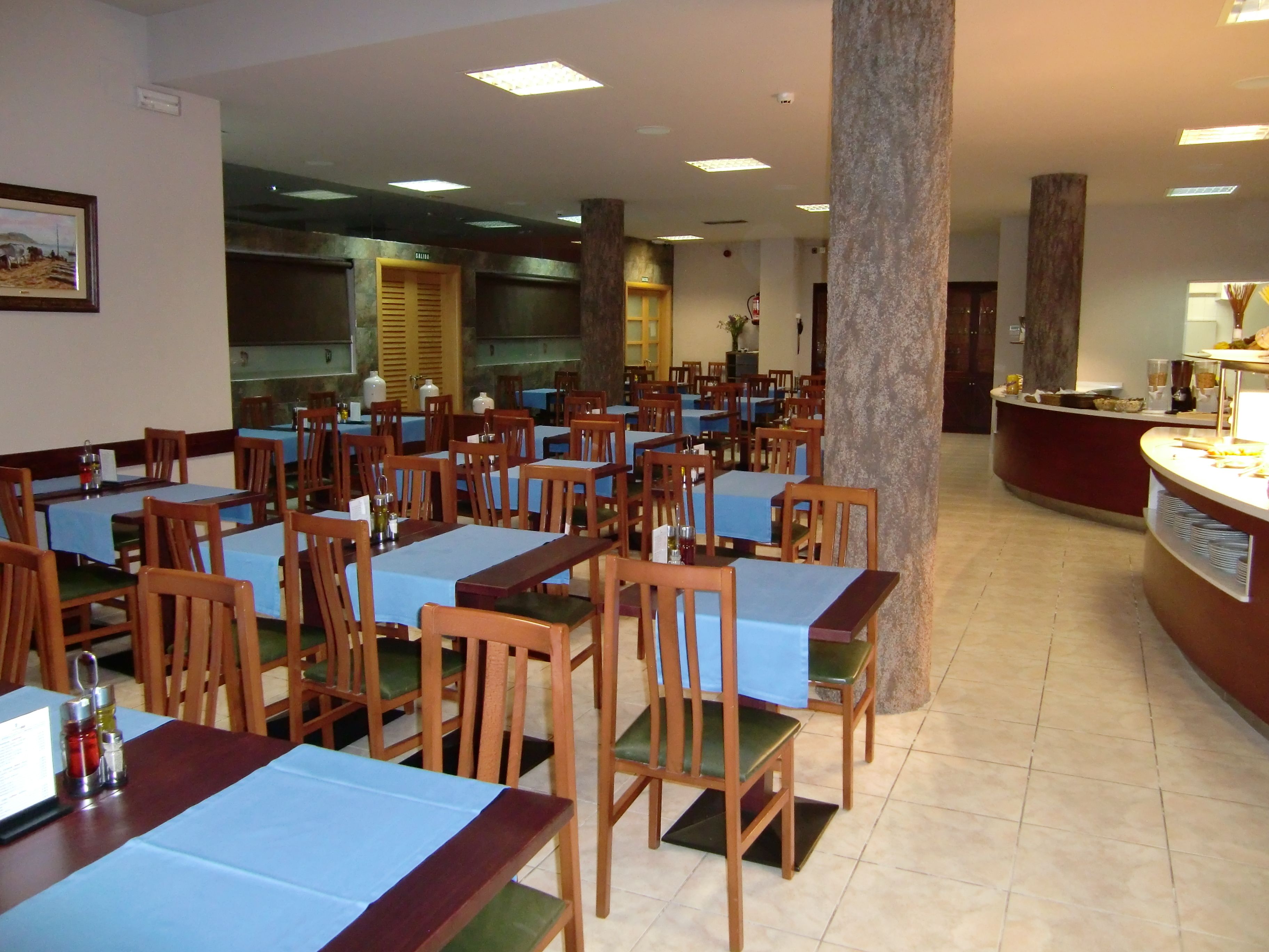 A restaurant with multiple tables and chairs, a kitchen area, and a counter with food items.