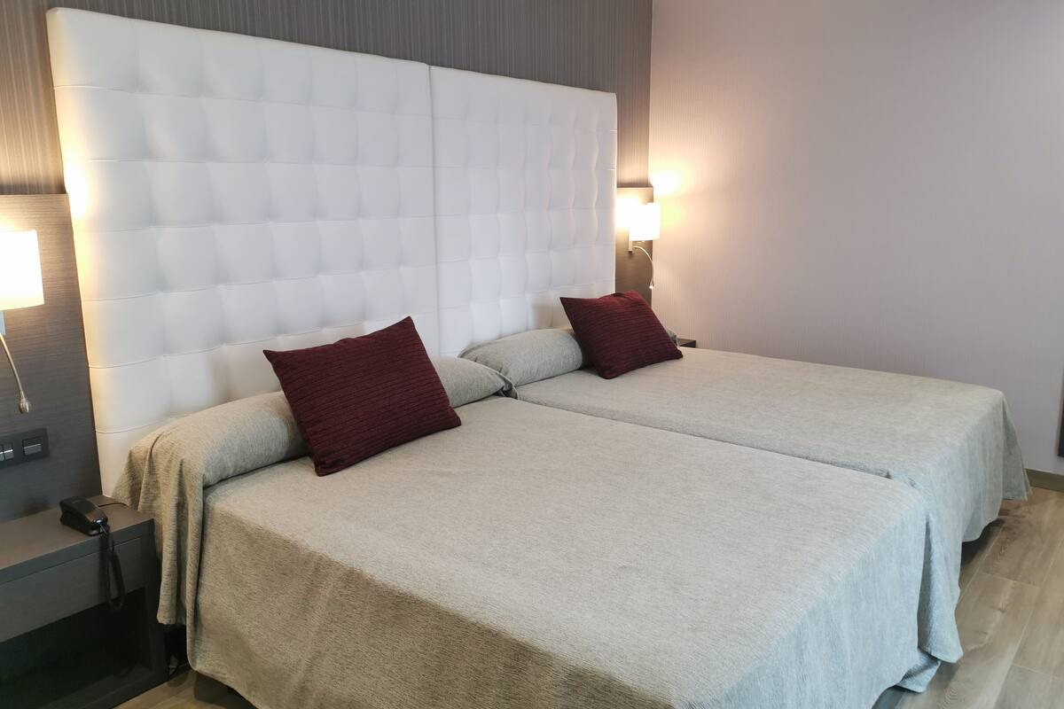 A double bed with a tufted headboard, two pillows, a bedside table with a lamp, and a nightstand with a phone.
