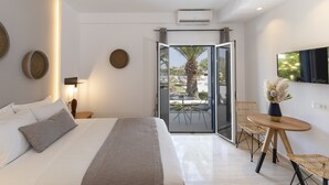 Ein modernes Hotelzimmer mit einem großen Bett, einem kleinen runden Tisch, Korbstühlen, einem Fernseher und einem Balkon mit einer Palme.
