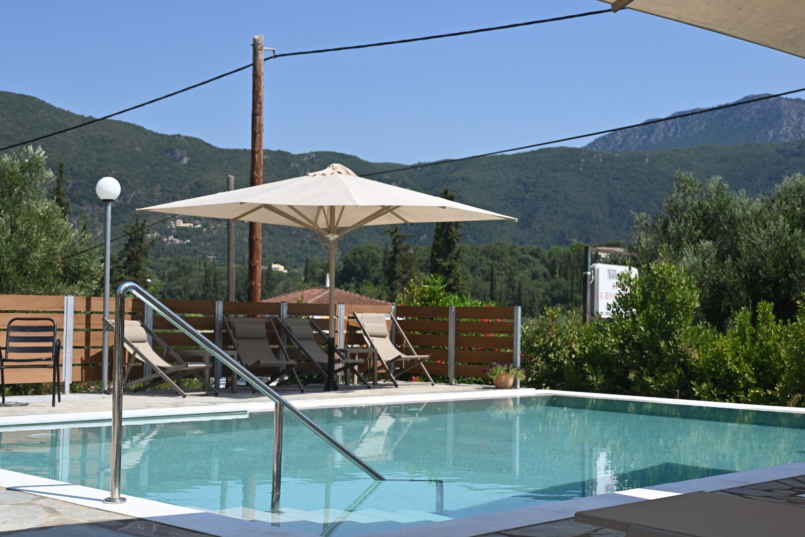En pool med liggestole, en parasol og udsigt til bjerge.