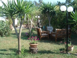 A garden with a wooden bench, a table, and chairs. There are potted plants and a lamp post. - Villa Avra (Corfu)