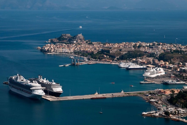 A coastal city with a historic fort, a marina with large cruise ships, and a mix of residential and commercial buildings. - Villa Avra (Corfu)