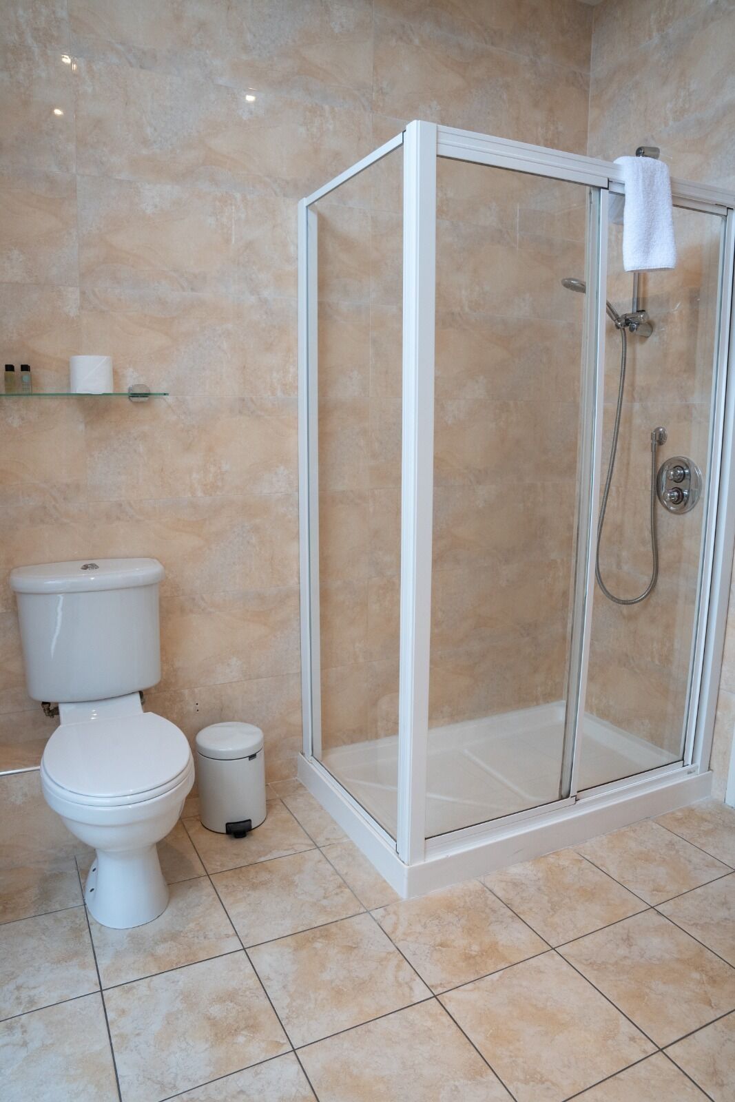 Un baño con ducha envuelta en vidrio, inodoro y cubo de basura.