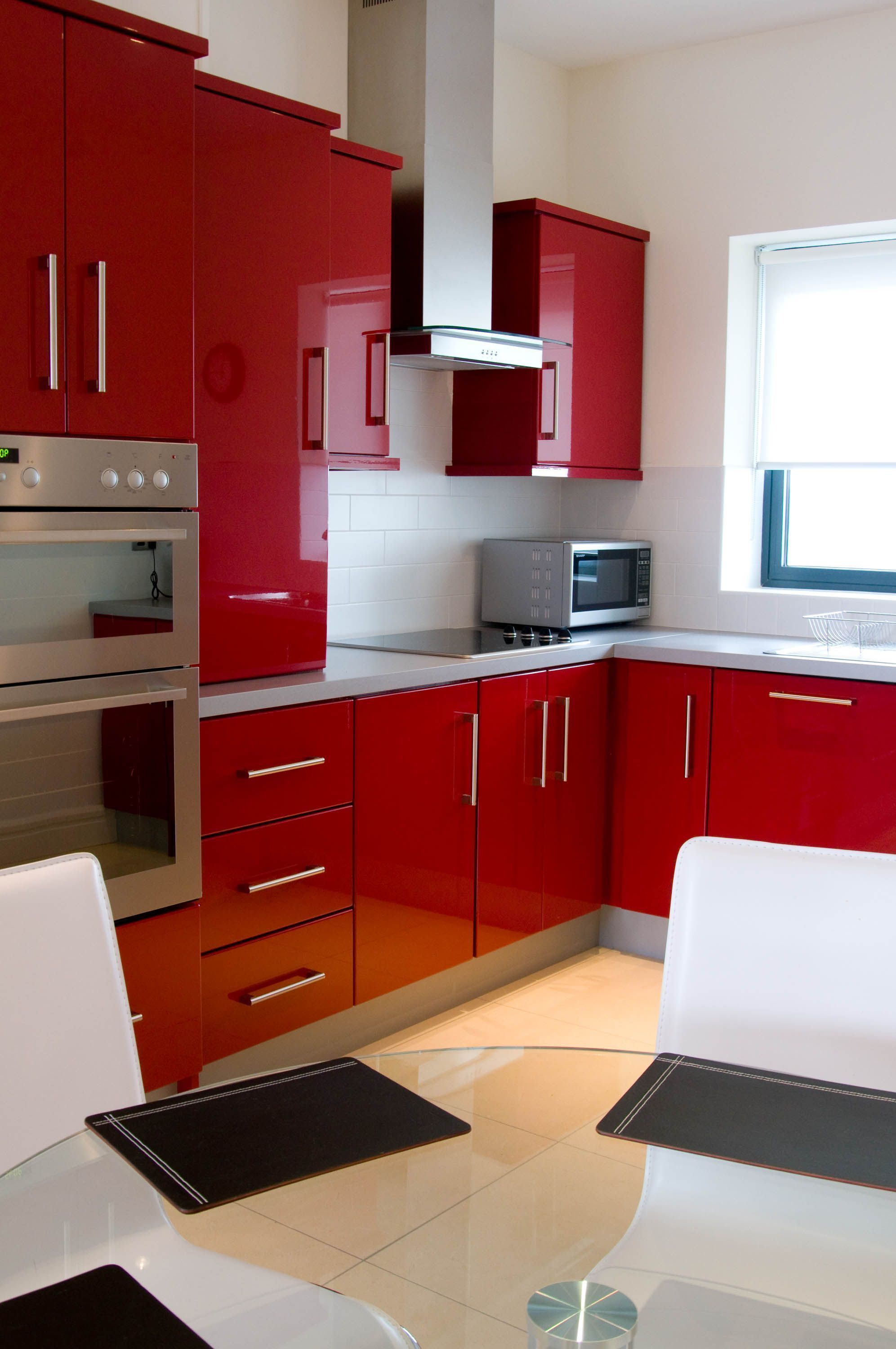 Une cuisine avec des meubles de rangement rouges, un four à micro-ondes et un four double.