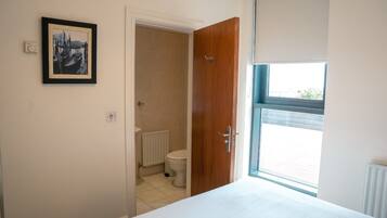 A bedroom with a bed, a wooden door, a window, and a bathroom visible through an open door.