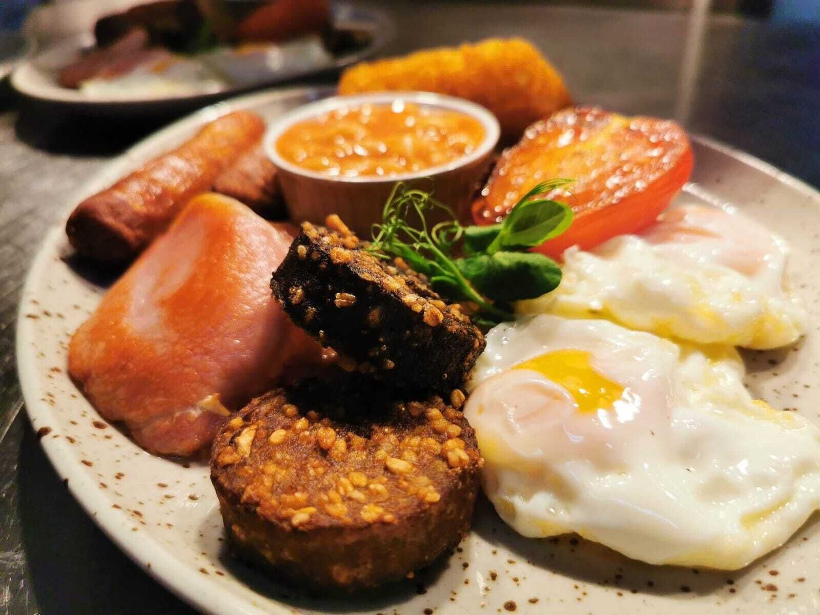 A plate of breakfast food including sausages, eggs, and a slice of tomato.