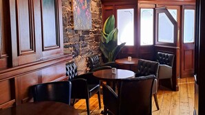 A restaurant interior with wooden tables and chairs, a stone wall, and a large window with a view. - Citypoint Apartments (Galway)