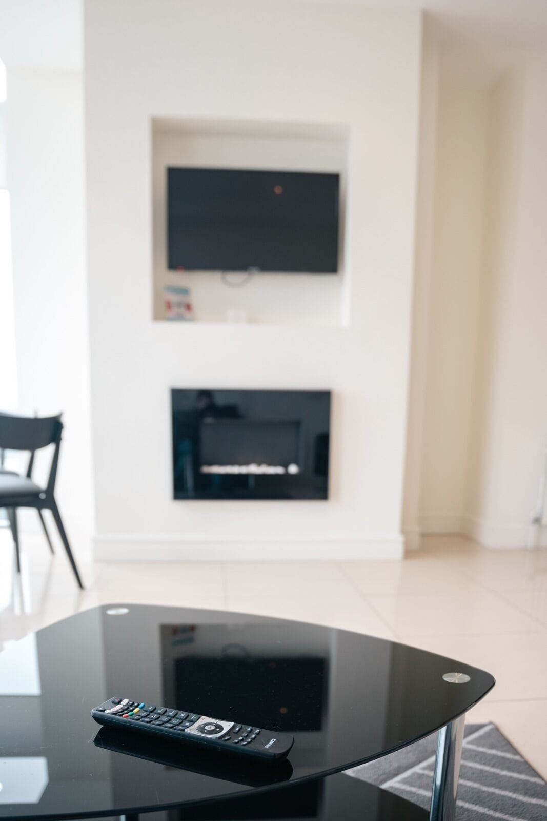 Un salon moderne avec une table basse en verre, une télécommande posée dessus et un téléviseur à écran plat fixé au mur, au-dessus d’une cheminée.