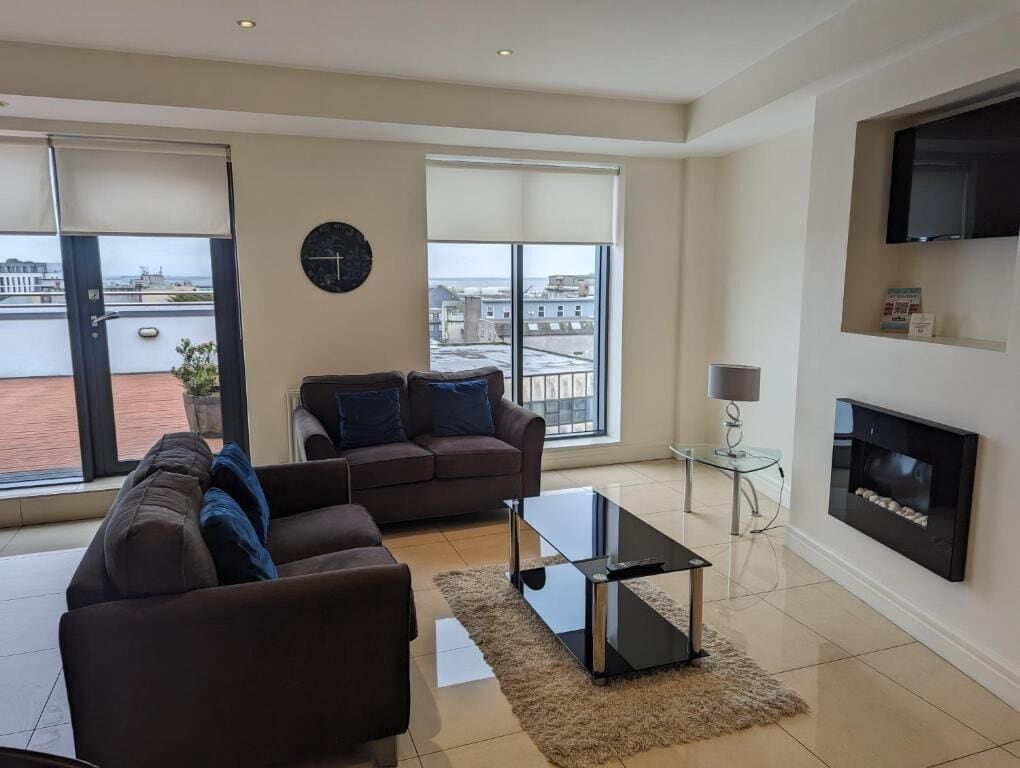 A modern living room with a sofa, a coffee table, a fireplace, and a TV mounted on the wall.