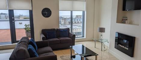 A modern living room with a sofa, a coffee table, a fireplace, and a TV mounted on the wall.
