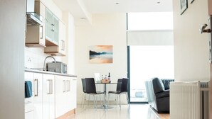 A modern kitchen with white cabinets and a dining area with a table and chairs. - Citypoint Apartments (Galway)