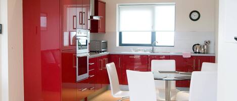 Una cocina moderna con armarios rojos, un horno de acero inoxidable y una zona de comedor con sillas blancas.