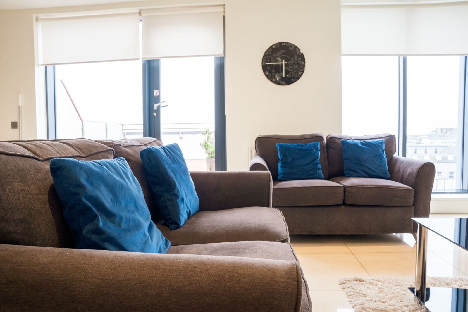 Ein Wohnzimmer mit zwei braunen Sofas, eines davon mit blauen Kissen, und einer runden Wanduhr.