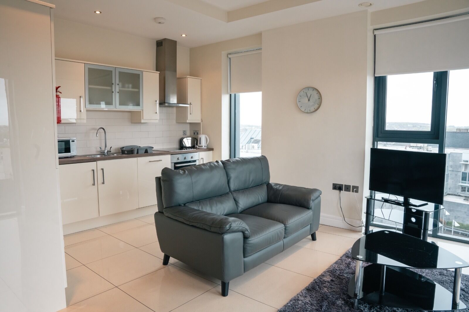 Un apartamento moderno con cocina, un sofá de cuero gris, televisor y vistas a la ciudad.