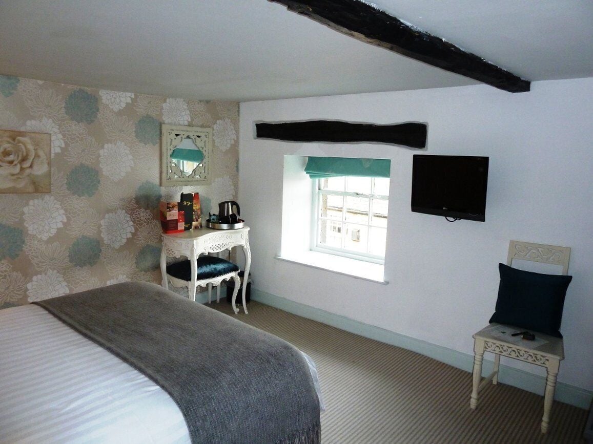 A bedroom with a bed, a dresser, a chair, a window, and a wall-mounted TV.