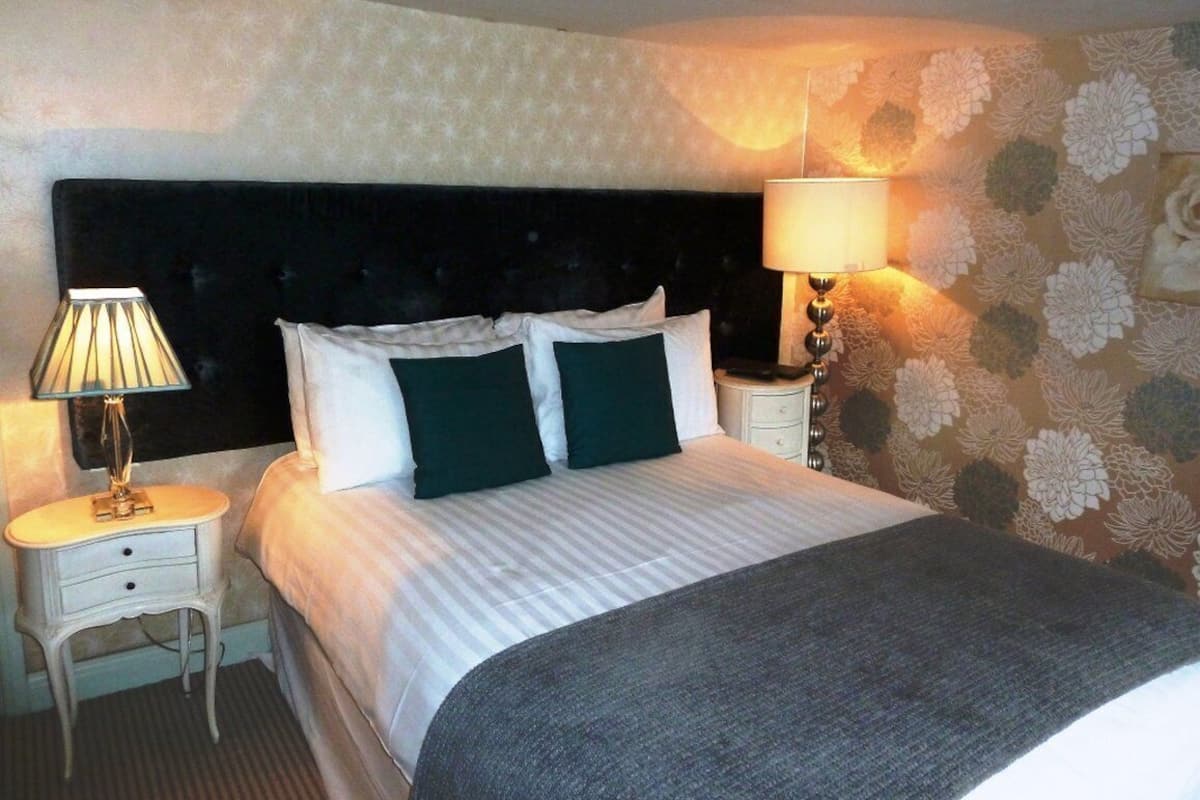 A neatly made bed with a dark headboard, two bedside lamps, and a floral-patterned wall.