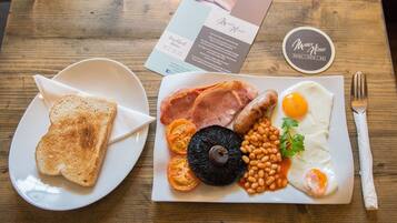 A breakfast plate with toast, eggs, sausages, beans, and tomatoes on a wooden table.
