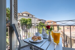 Un balcón con una mesa dispuesta para el desayuno, que incluye cruasanes, tazas de café y un vaso de zumo de naranja.