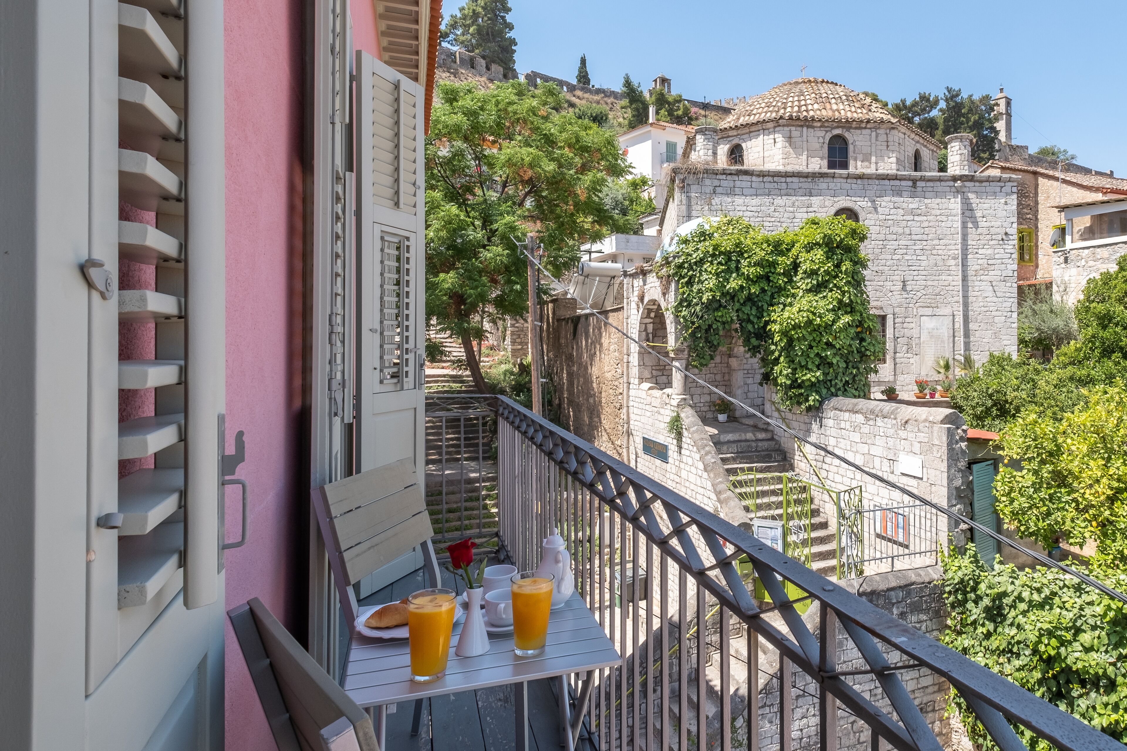 A balcony with a table set for breakfast, overlooking a stone building with a dome and a staircase.