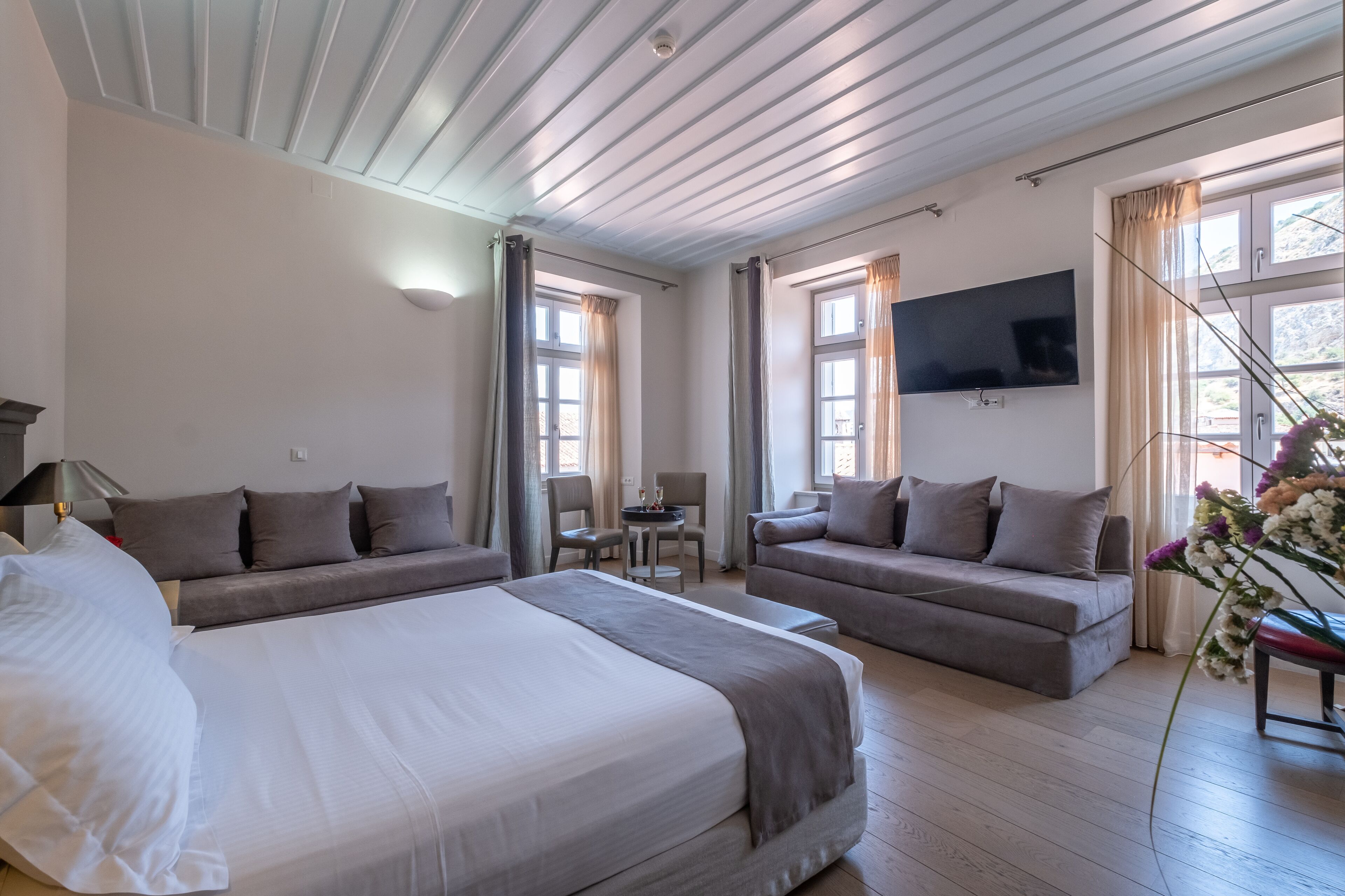 A hotel room with a large bed, two sofas, a TV, and a small table.