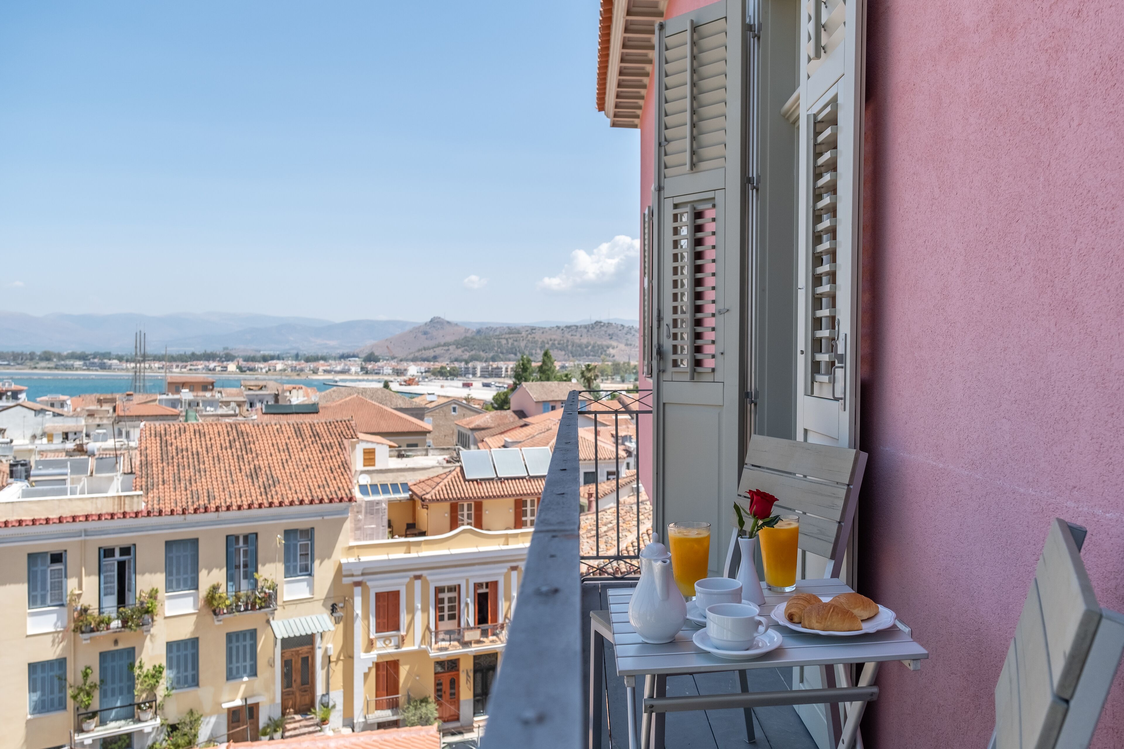 A balcony with breakfast setup overlooking a coastal cityscape.