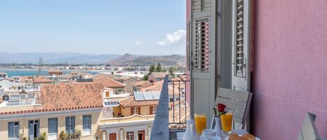 A balcony with breakfast setup overlooking a coastal cityscape.